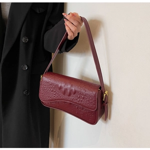 Détail d'un sac sous le bras rouge vin avec motif crocodile et texture cuir de luxe