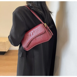 Détail du sac sous le bras à motif crocodile bordeaux sur un mannequin en costume noir