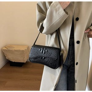 Détail d'un sac à bandoulière noir motif crocodile avec boucle dorée et rabat chic