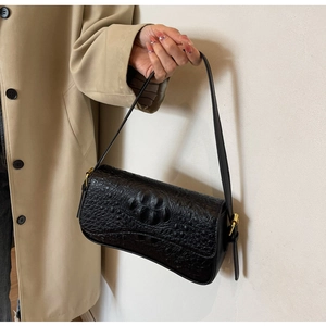 Détail du sac baguette noir texture crocodile avec boucle en métal doré sur la bandoulière