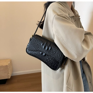Gros plan du sac sous le bras noir à motif crocodile porté avec un trench beige