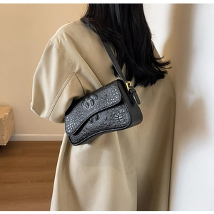 Détail du sac bandoulière noir en cuir embossé crocodile avec boucle dorée sur modèle