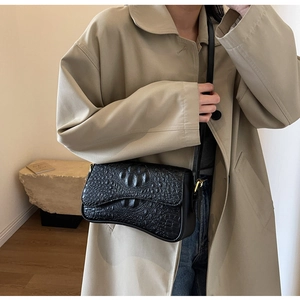 Détail du sac à bandoulière noir motif crocodile avec rabat magnétique et boucle dorée