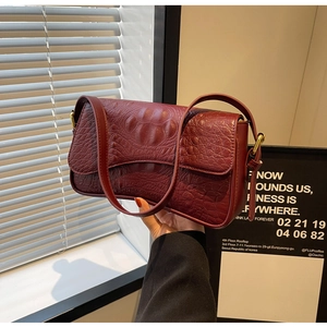 Détail de la texture cuir crocodile rouge foncé sur un sac porté épaule élégant