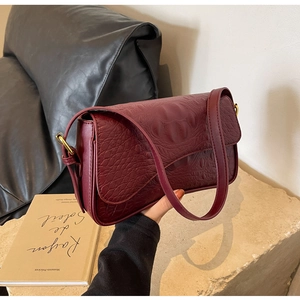 Gros plan sur la texture crocodile bordeaux et la boucle dorée du sac à bandoulière chic