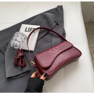 Détail du sac sous le bras bordeaux à motif crocodile avec garniture dorée et deux anses