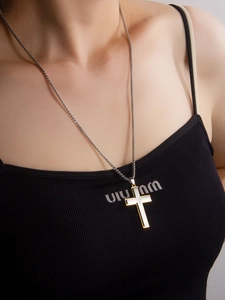 Gros plan d'un collier pendentif croix bicolore avec diamants porté sur un débardeur noir
