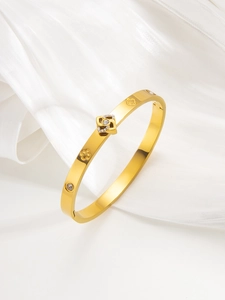 Macro detail of gold clover bangle with micro-pave crystals on white silk background