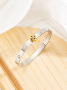 Detail of silver clover bangle with gold crystal charm on wooden and fabric background