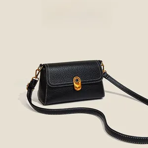 Close-up of black litchi leather bag with gold clasp and white contrast stitching