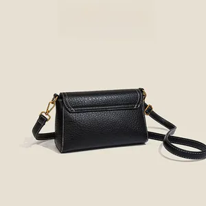 Detail of black lychee leather crossbody bag with white contrast stitching and gold hardware