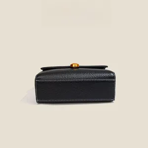 Detail of black lychee grain leather bag with white stitching and gold metal buckles