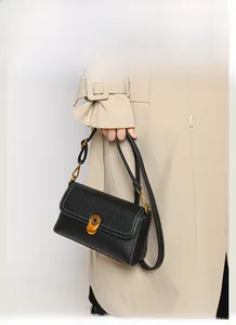 Detail of black litchi texture leather handbag with gold oval clasp on a beige coat