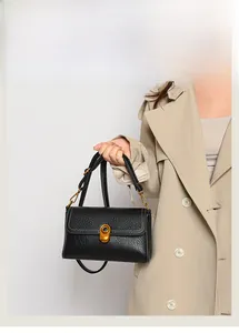 Detail of black lychee leather crossbody bag with gold oval twist lock and white stitching