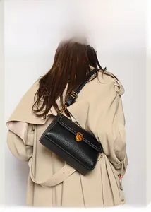 Detail of a black pebbled leather crossbody bag with a gold twist-lock and beige trench coat