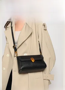 Detail of black lychee leather crossbody bag with gold twist lock and contrast stitching