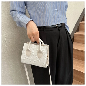 Detail of white mini handbag featuring textured floral jacquard fabric and slim handles