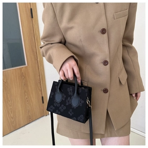 Detail of black mini square bag featuring floral texture and golden metal hardware