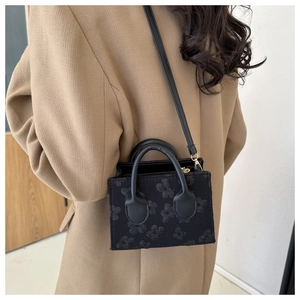 Detail of black square handbag with 3D floral embossing texture on wool coat