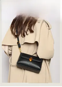 Detail of black pebbled leather crossbody bag with gold buckle and white stitching