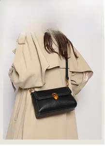 Detail of black pebbled leather crossbody bag with gold buckle and white stitching