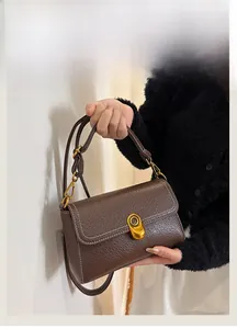 Detail of dark brown lychee pattern leather bag with golden oval buckle and white stitching