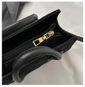 Detailed close-up of golden metal zipper and embossed floral pattern on black handbag