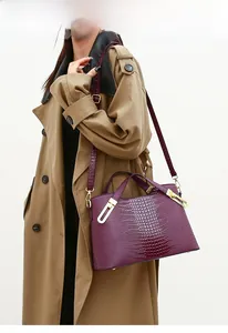 Detail of burgundy crocodile pattern handbag with gold hardware on a trench coat model