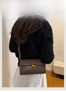 Close-up of vintage brown pebble leather shoulder bag with golden twist lock on a model