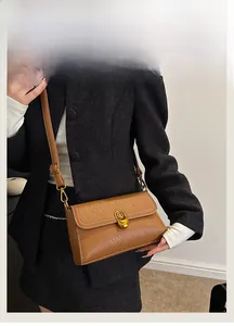 Close-up of brown litchi leather bag with golden metal buckle on model in dark blazer