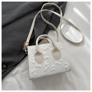 Close-up of white floral textured mini bag with cream handles and gold hardware
