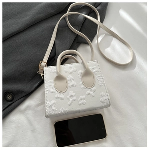 Detailed macro of white floral texture on mini square handbag next to smartphone for scale