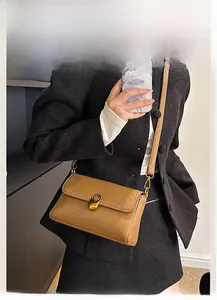 Detailed close-up of tan textured leather shoulder bag with golden metallic clasp