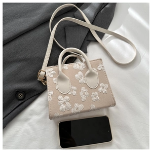 Top view of beige mini crossbody bag with white flower embroidery next to a smartphone