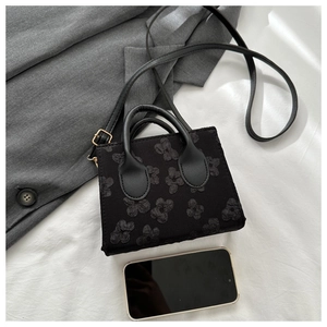 Chic black mini crossbody bag with 3D floral relief pattern on grey blazer background
