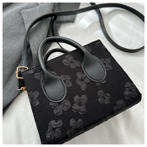 Detail of black mini tote bag with 3D floral texture, leather handles and gold metal hardware