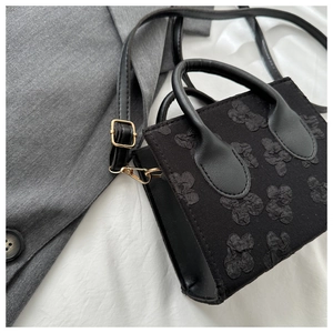 Detail view of small black handbag featuring 3D floral texture and gold hardware accents