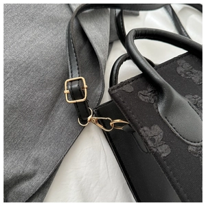 Close-up of golden metal hardware and black textured floral fabric on small square bag