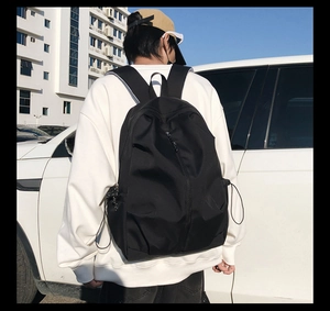 Detailed outdoor street view of a black multi-pocket backpack with drawstring side pockets