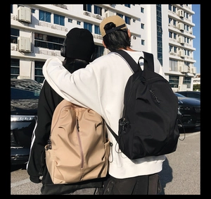 Outdoor lifestyle shot of two models wearing minimalist khaki and black nylon backpacks