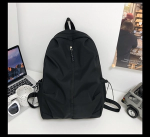 Detail of a black minimalist backpack with front zipper pocket and drawstring side pockets
