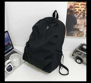 Close-up of black minimalist backpack with side drawstring pocket on a white desk