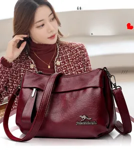Détail du sac à main bordeaux en cuir grainé avec logo kangourou sur veste en tweed