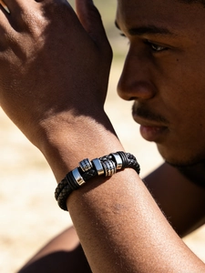 Close-up of men's braided black leather bracelet with silver metal charms and texture