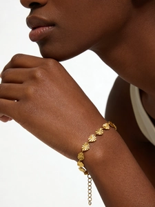 Detail of gold heart link bracelet with sunburst texture on a woman's wrist