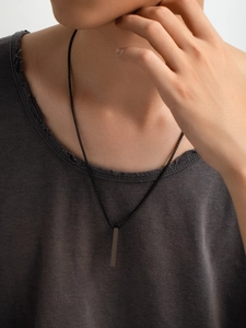Detail of a minimalist black vertical bar pendant on a box chain worn by a male model