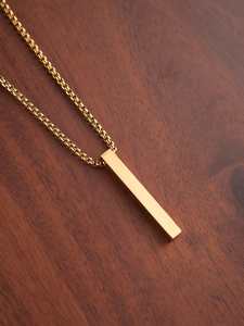 Close-up of polished gold rectangular bar pendant necklace on a dark walnut wood surface