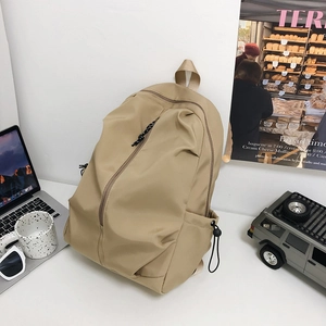Large khaki school backpack with diagonal zipper and drawstring side pocket on a desk