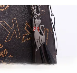 Detail of silver cat charm with red bowtie and leather tassels on monogram printed tote bag