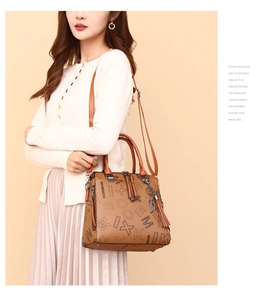 Detailed view of brown letter print tote with tassel charm on neutral background